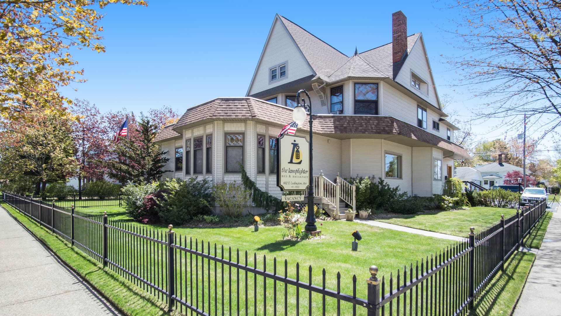 A large, charming house with a landscaped yard and an iron fence, featuring a sign and American flags.