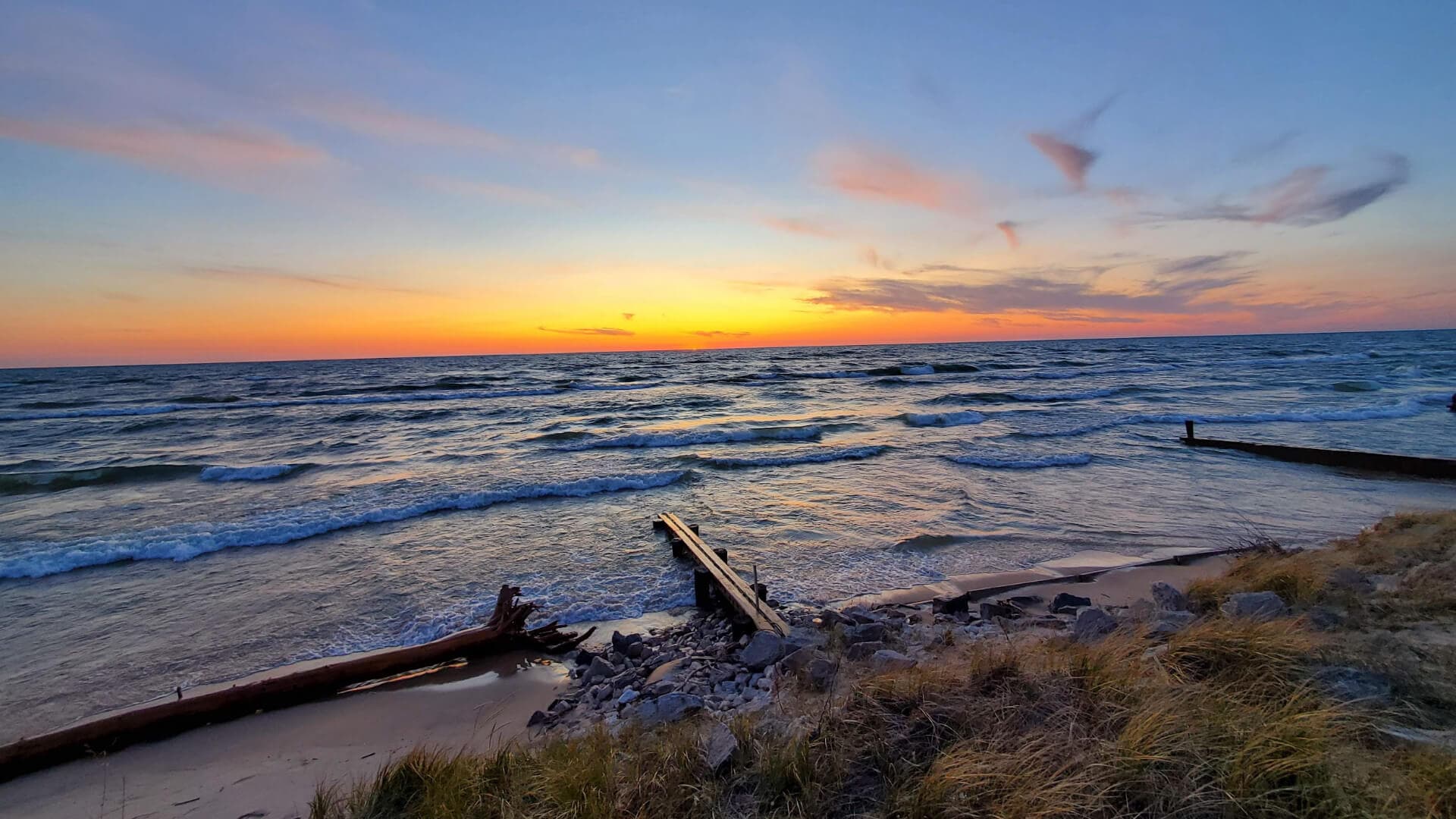 A serene beach scene at sunset, with gentle waves lapping at the shore and a colorful sky.