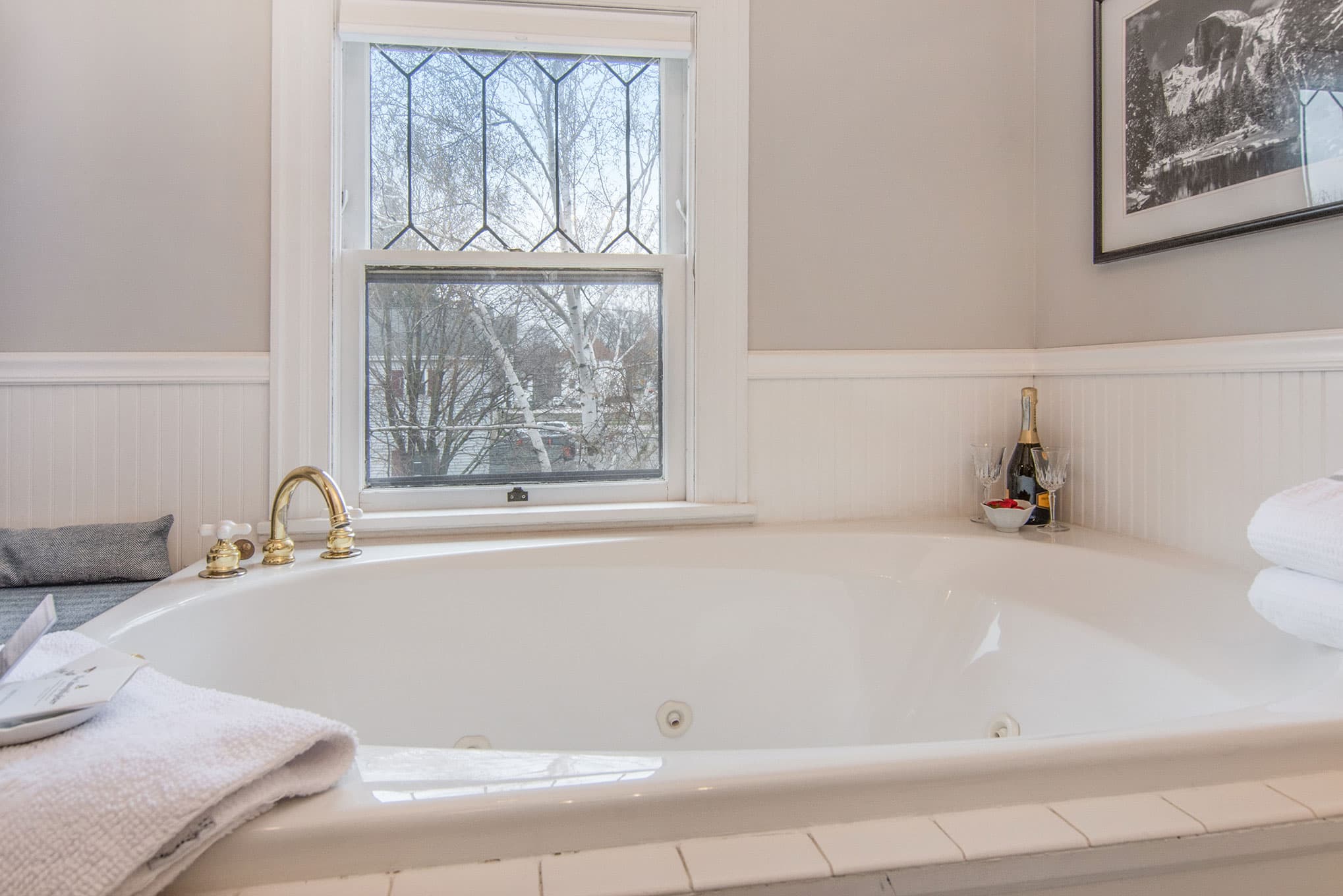 A luxurious bathtub next to a window, accompanied by champagne and towels.