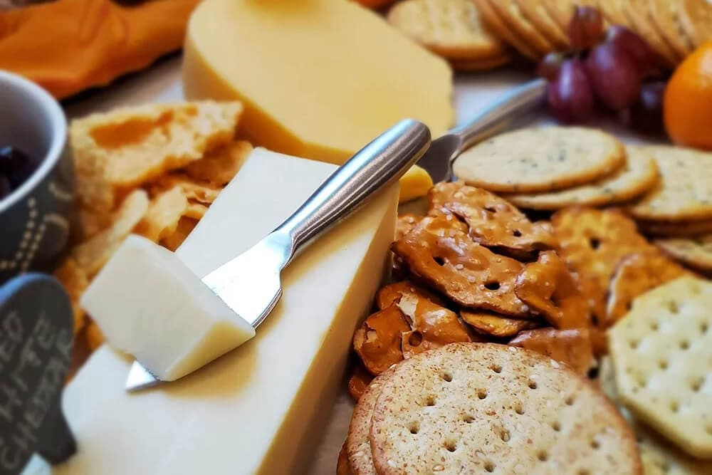 A spread of cheeses, crackers, pretzels, and fruits arranged on a platter.