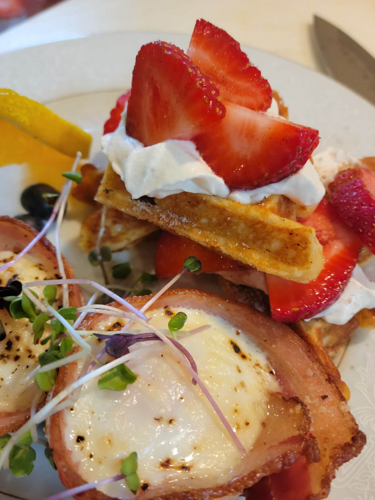 A plate of waffles topped with strawberries, whipped cream, and two baked eggs wrapped in bacon.
