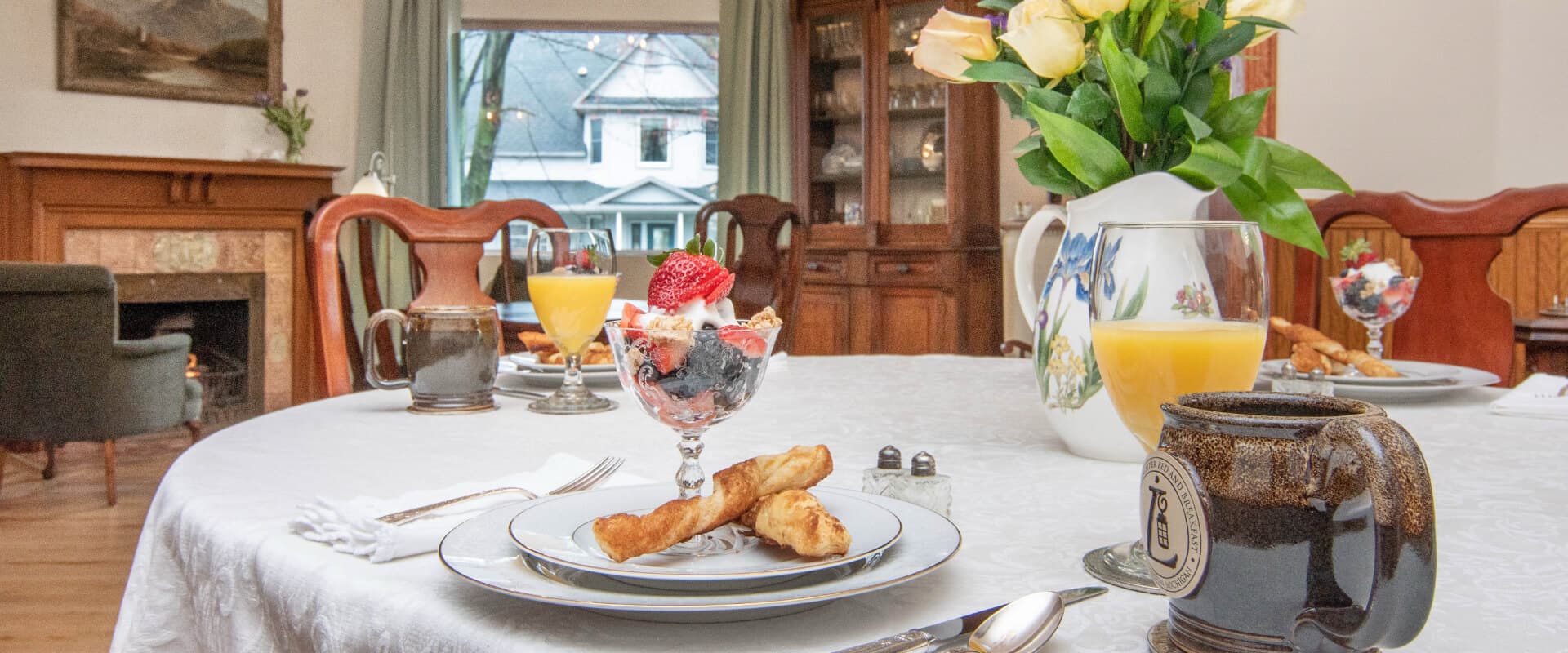 A beautifully set dining table with a dessert, drinks, and a bouquet of flowers in a cozy room.
