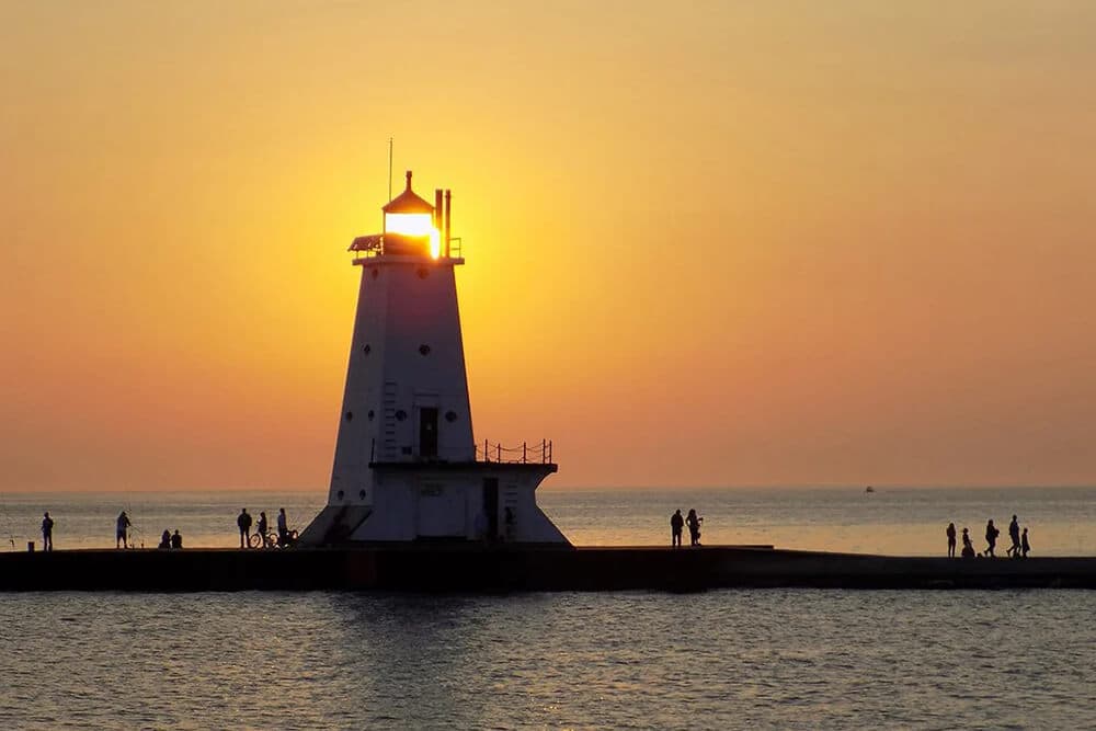 A silhouette of a lighthouse against a vibrant sunset, with people walking along the pier.