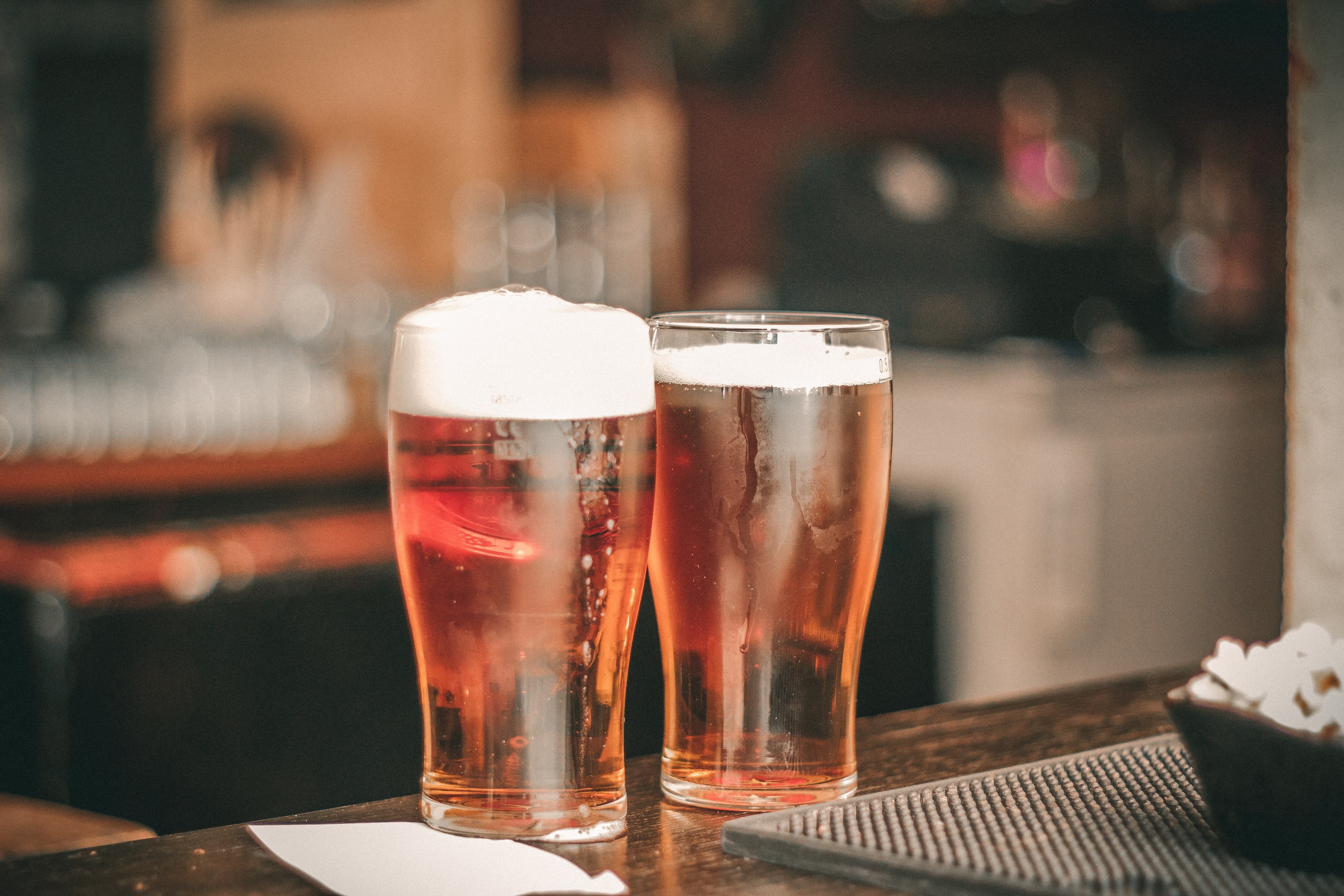 Two glasses of beer sit on a wooden bar. Two glasses of beer sit on a wooden bar.