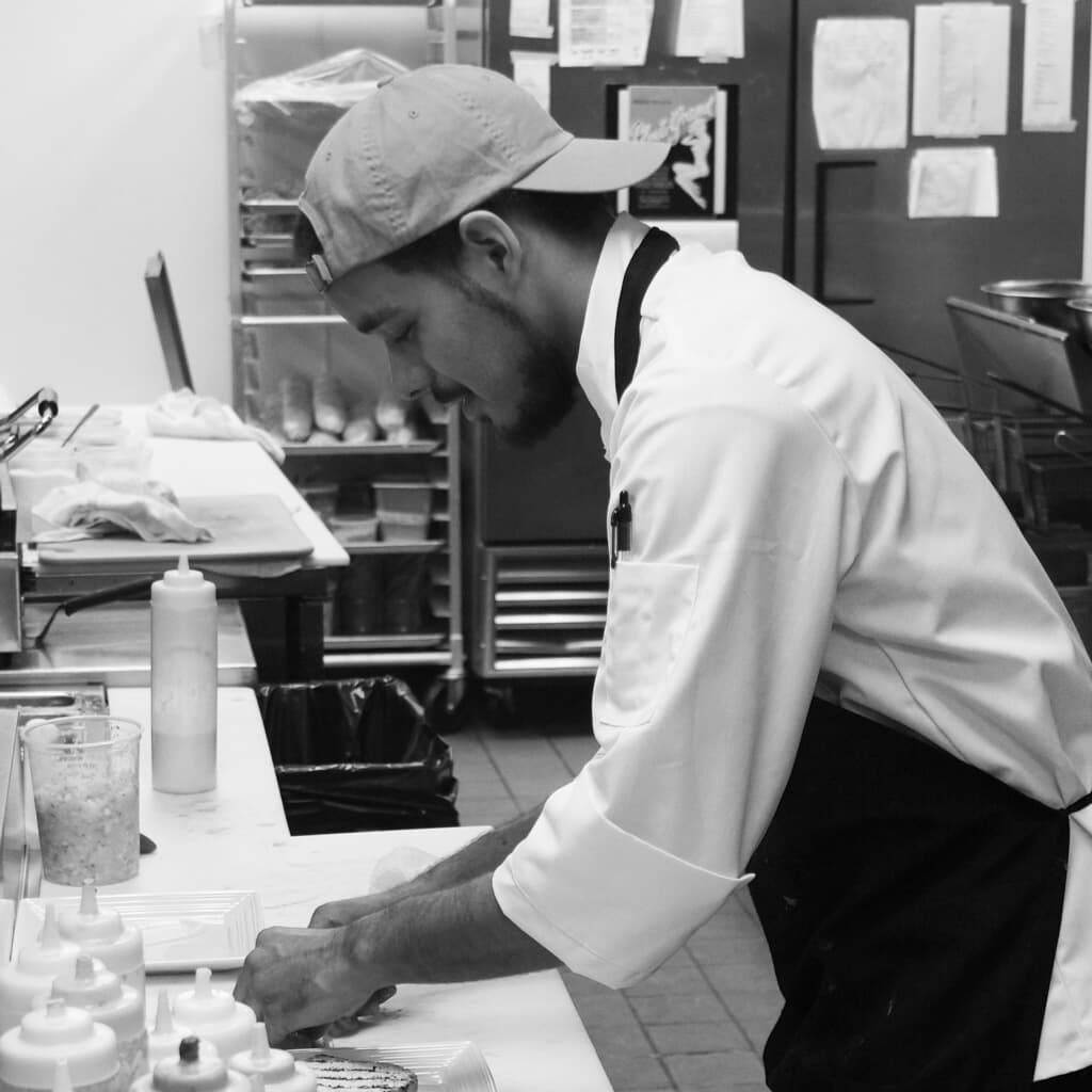A young chef carefully plates food in a kitchen.