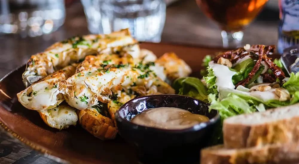 A plate of grilled shrimp with a side of salad, dipping sauce, and bread.