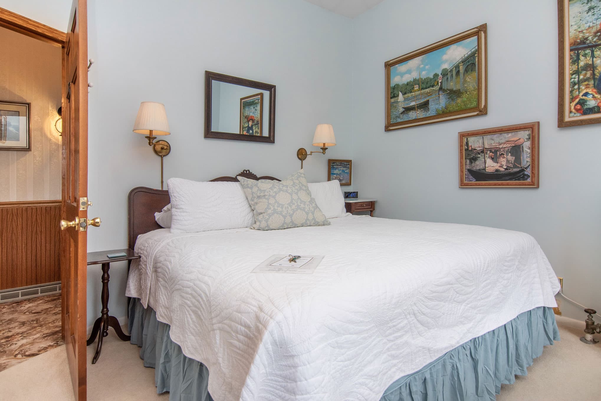 Cozy bedroom featuring a queen bed, decorative pillows, and art on pastel blue walls.