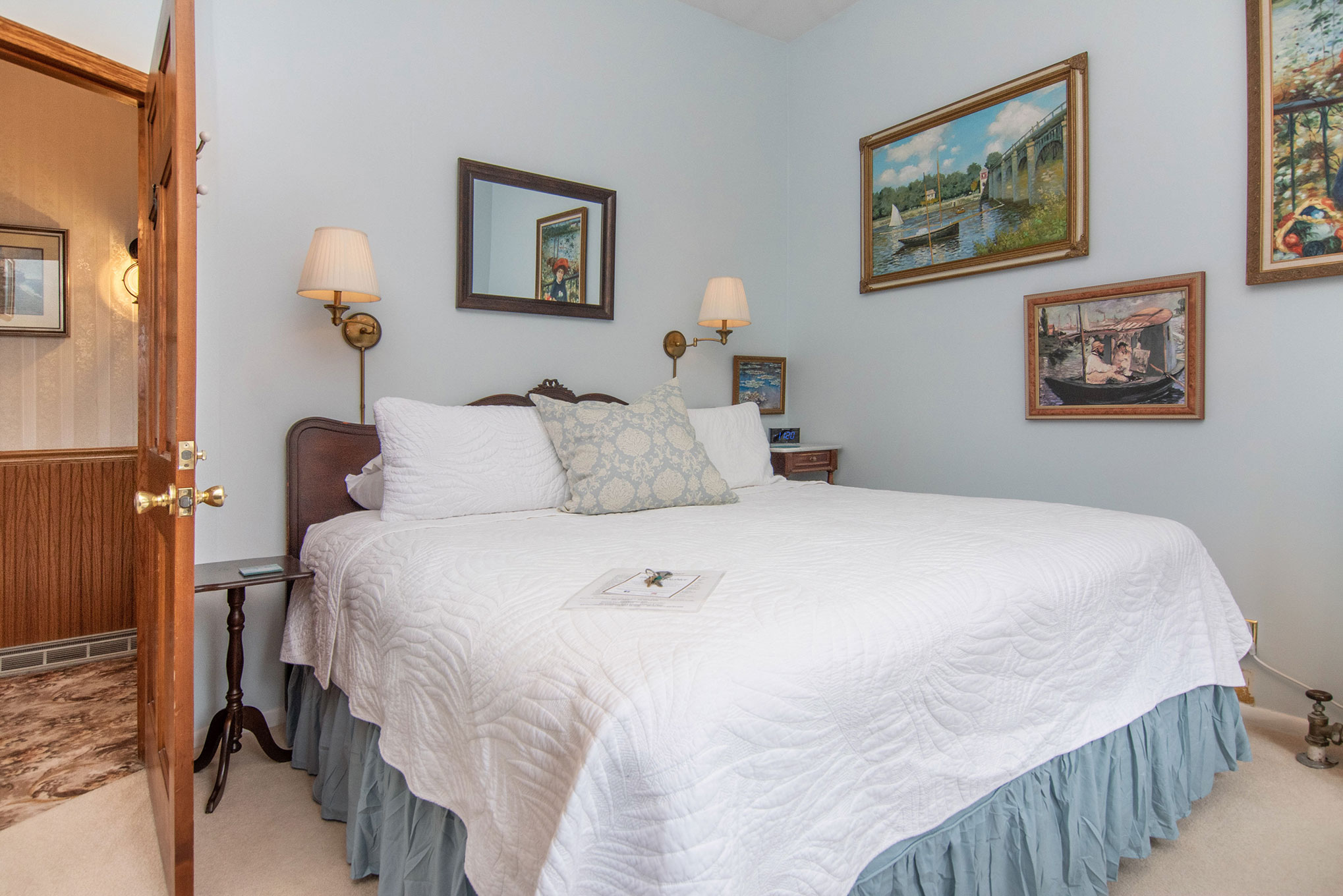 Cozy bedroom featuring a queen bed, decorative pillows, and art on pastel blue walls.