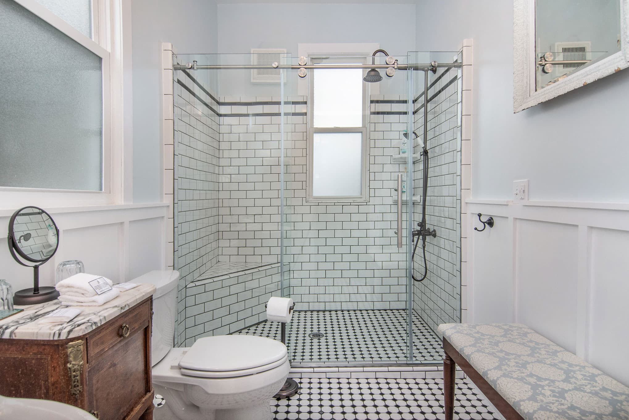 A modern bathroom featuring a glass shower, white tiled walls, and a decorative bench.