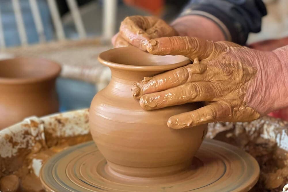 A potter shapes a clay vase on a spinning wheel.