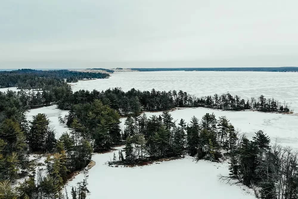 Aerial view of snow-covered land and a frozen lake surrounded by evergreen trees.