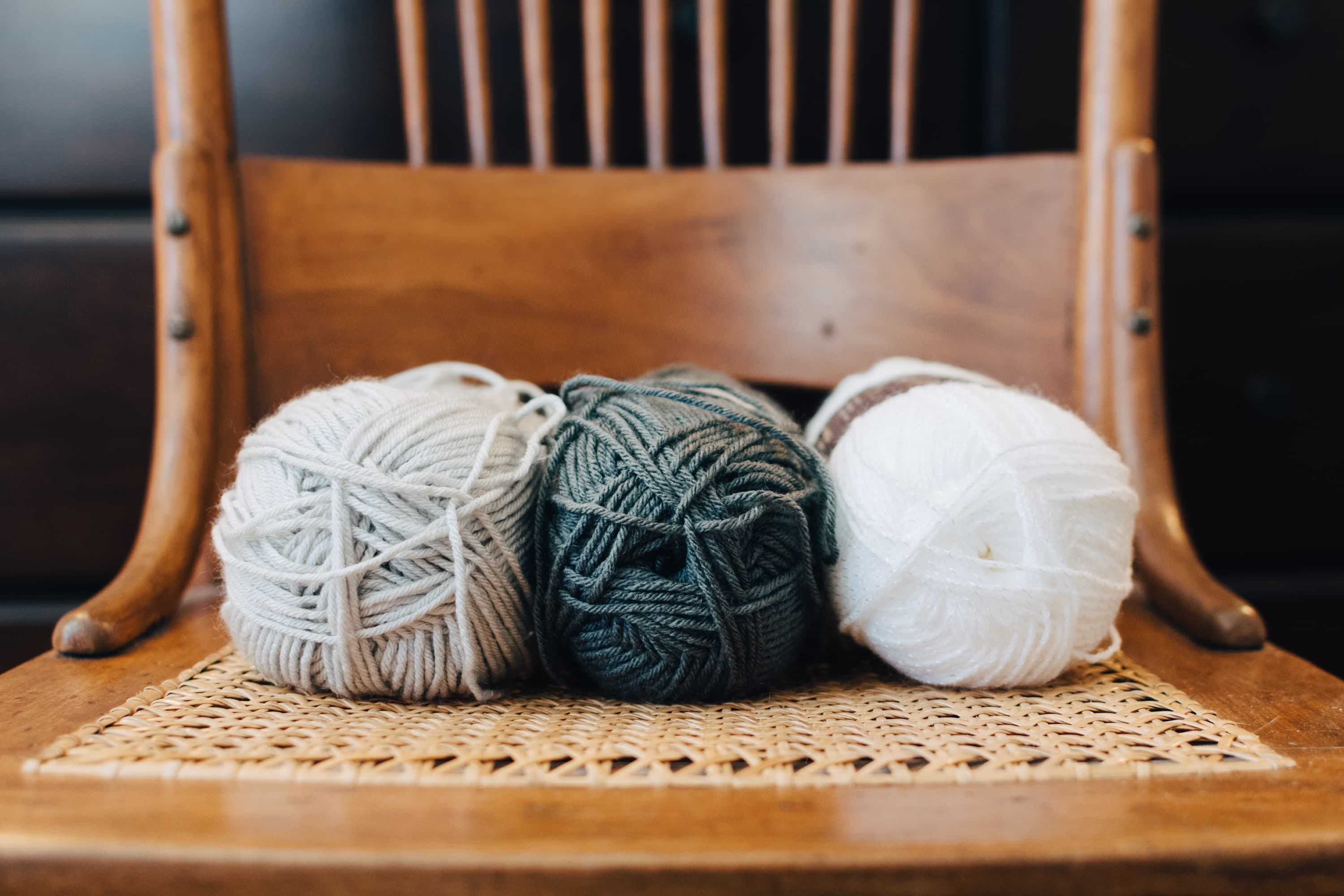 Three balls of yarn in gray, green, and white rest on a wooden chair. Three balls of yarn in gray, green, and white rest on a wooden chair.