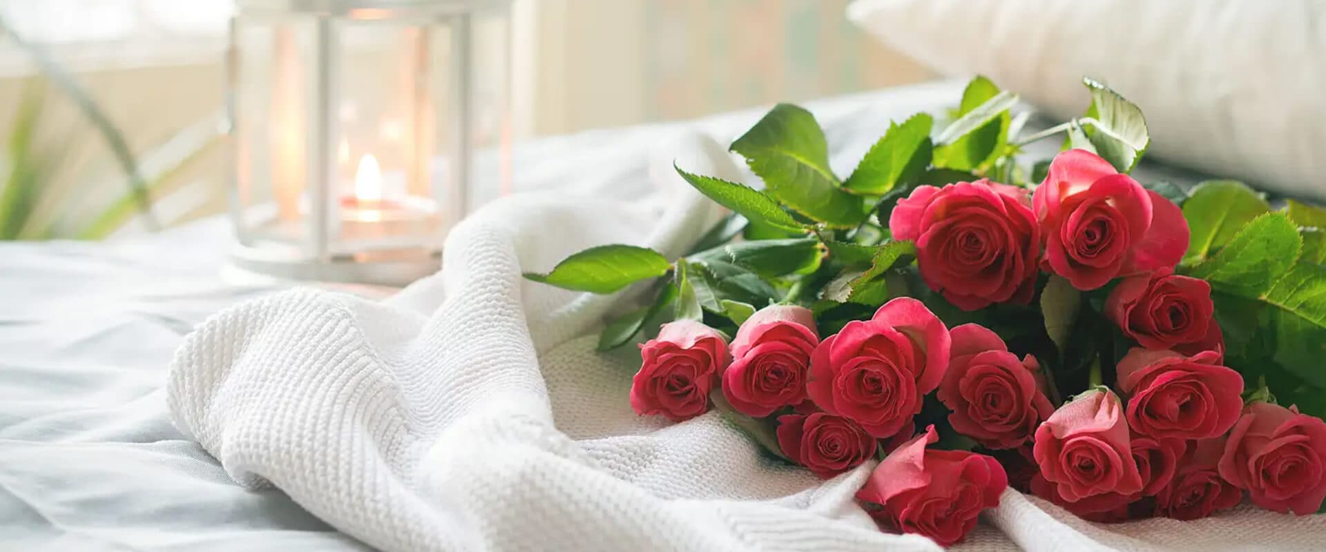 A bouquet of red roses resting on a soft white blanket beside a candle.