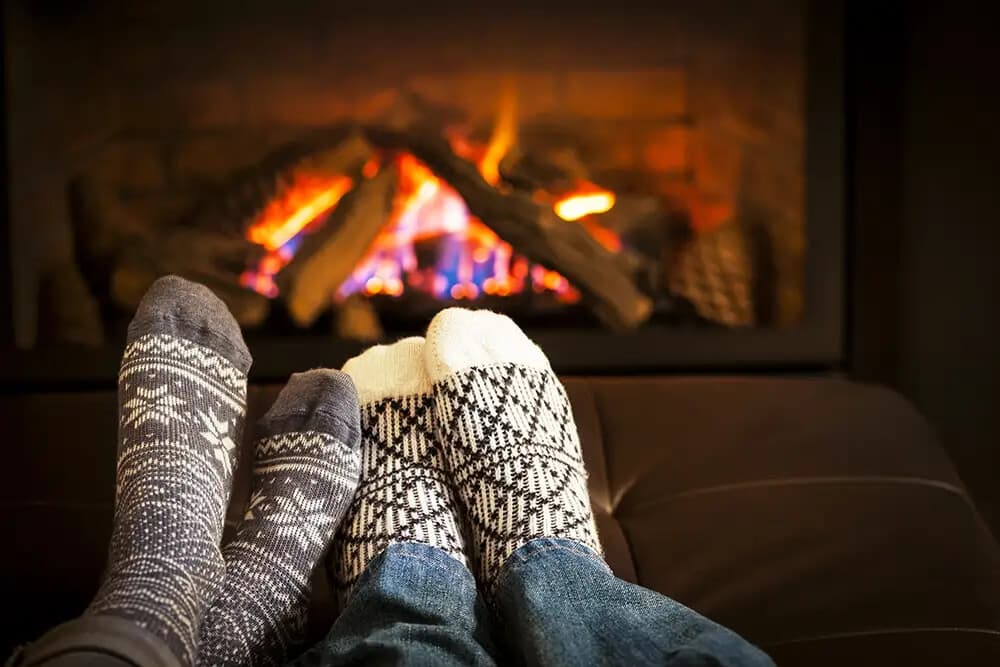 Cozy feet in patterned socks resting in front of a warm fireplace.