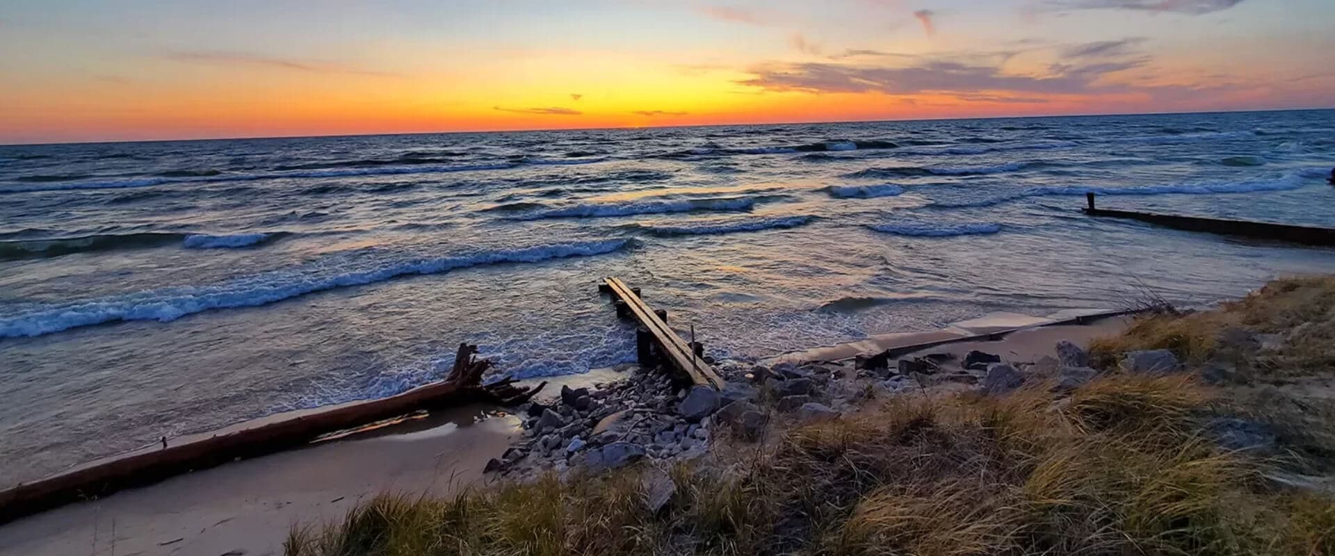 A serene beach scene at sunset, with gentle waves and a weathered wooden structure along the shore.