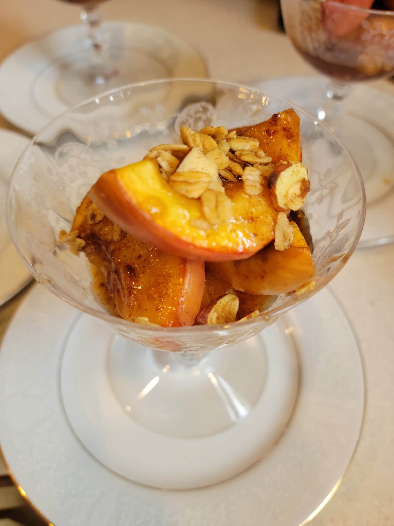 A glass dessert bowl filled with caramelized apple slices topped with toasted oats.