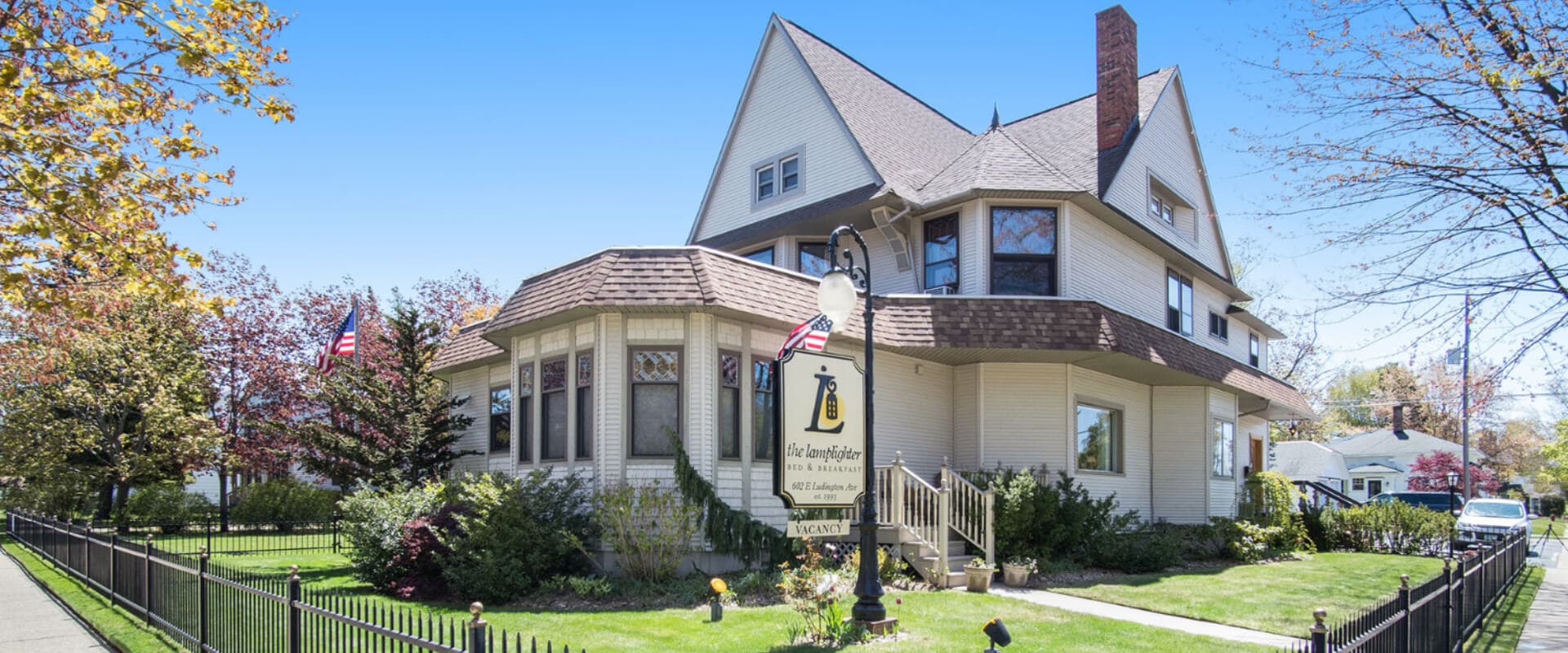 A charming, multi-story house with a decorative sign and American flags in a well-kept yard.